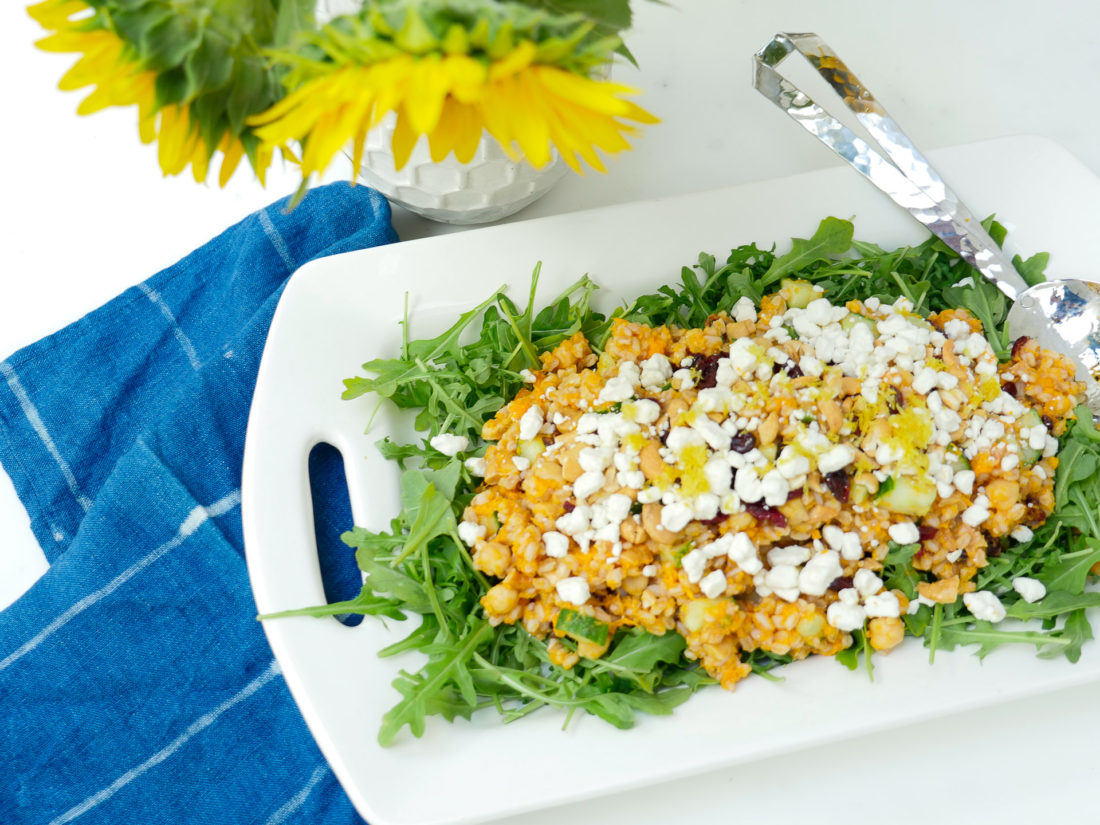 Happily Brenda After Autumn Farro Salad with Sweet Potato, Cucumber, Chickpeas, cranberries, goat cheese, cashews, arugula, and lemon zest phtographed in a marble kitchen with a blue shibori dyed tea towel and sunflowers