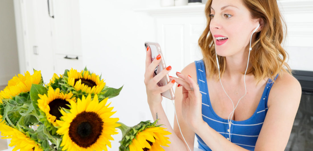 Brenda Mierish Martino of blog Happily Brenda After sitting at her kitchen table next to a vase of sunflowers, wearing a striped blue and white maternity tank and listening to an audiobook on Audible