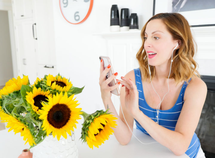 Brenda Mierish Martino of blog Happily Brenda After sitting at her kitchen table next to a vase of sunflowers, wearing a striped blue and white maternity tank and listening to an audiobook on Audible