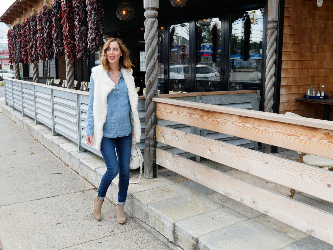 Brenda Mierish Martino of lifestyle blog Happily Brenda After wearing dark denim maternity jeans, a light chambray maternity top, white vest, and light brown western style booties walking down the street in connecticut