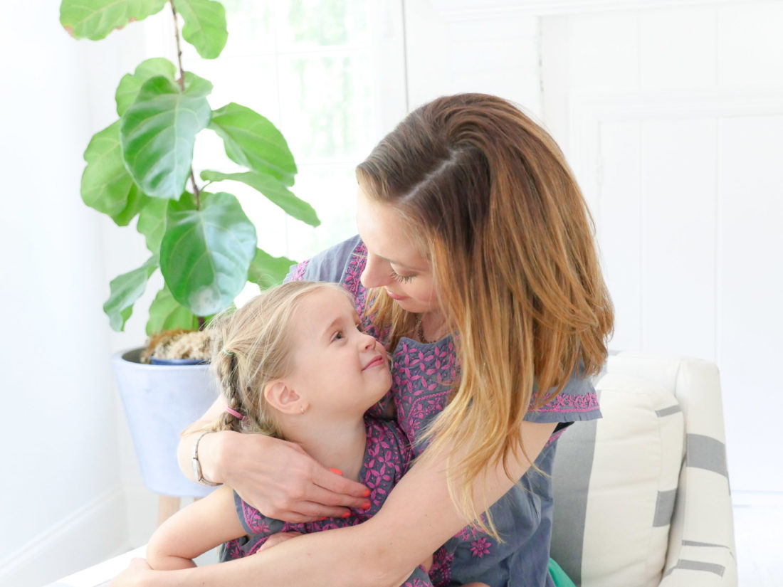 Brenda Mierish Martino and Marlowe Martino wear matching embroidered dresses and sit together in a striped armchair in the family room of their Connecticut home
