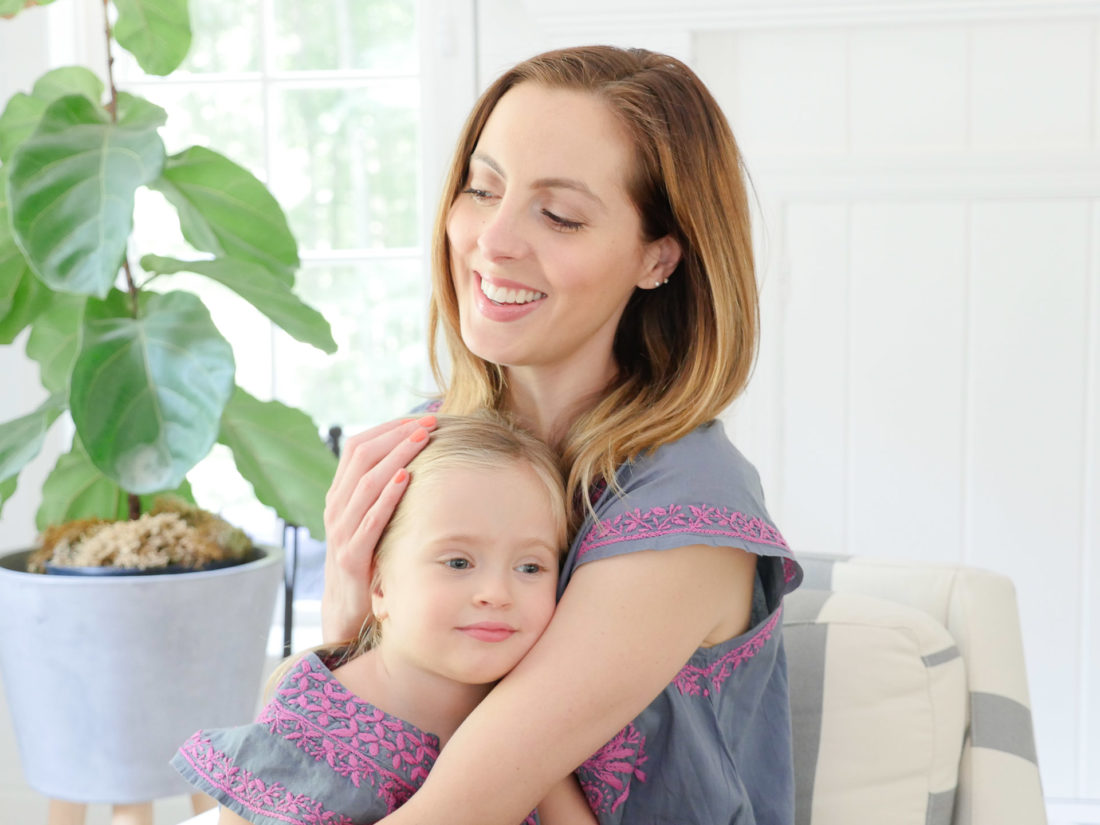 Brenda Mierish Martino and Marlowe Martino wear matching embroidered dresses and sit together in a striped armchair in the family room of their Connecticut home