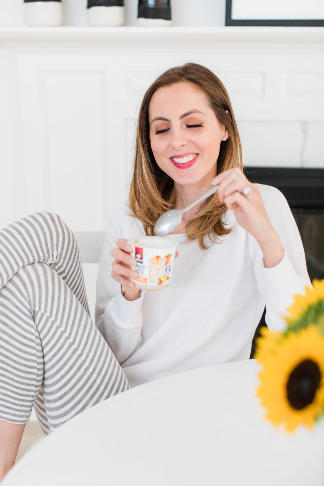 Brenda Mierish Martino sits at the kitchen table in a pair of grey and white striped pajamas and eat breakfast next to a vase of sunflowers