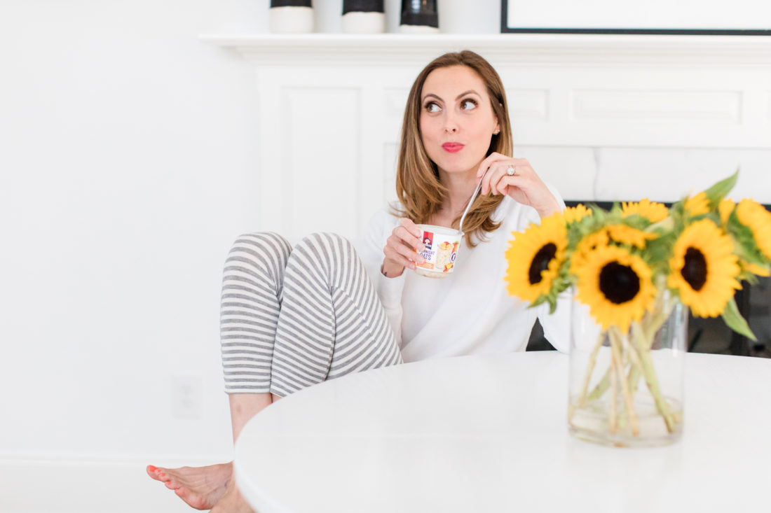 Brenda Mierish Martino sits at the kitchen table in a pair of grey and white striped pajamas and eat breakfast next to a vase of sunflowers