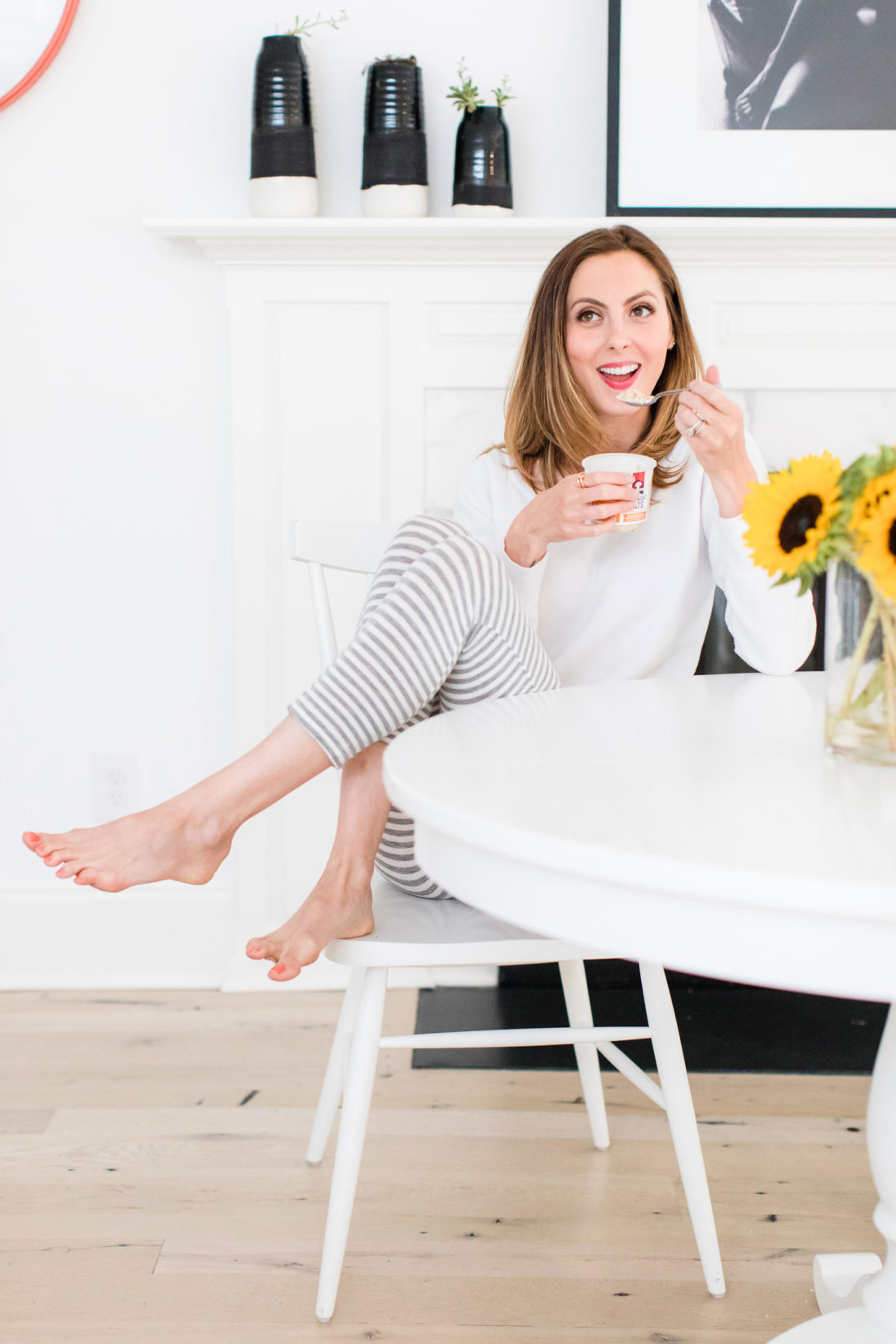 Brenda Mierish Martino sits at the kitchen table in a pair of grey and white striped pajamas and eat breakfast next to a vase of sunflowers