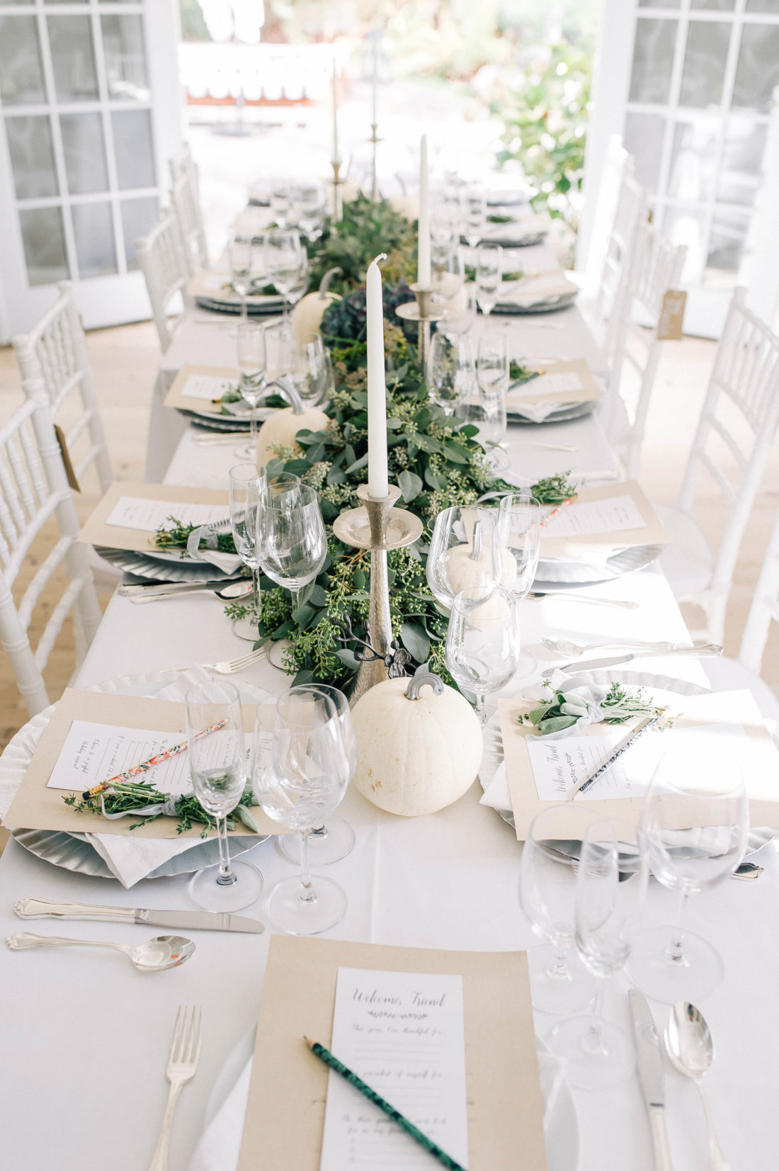 Crisp and modern white, flax, and silver tablescape at Brenda Mierish Martino's Friendsgiving, featuring a long eucalyptus garland and white pumpkins