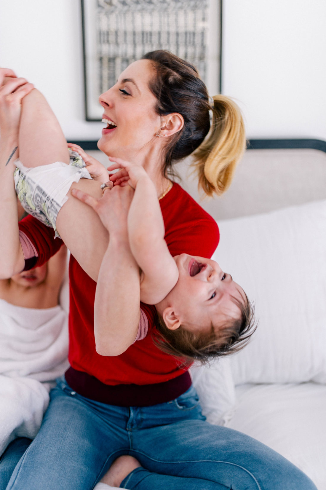 Brenda Mierish Martino wears a red sweater and jeans, and lifts one year old son, Major, in the air to tickle him