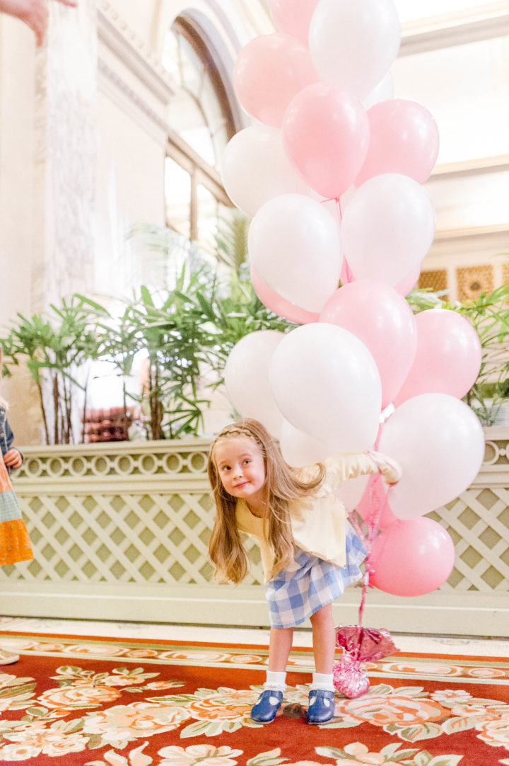 Brenda Mierish Martino's daughter Marlowe carries pink and white balloons while walking through the iconic Plaza Hotel